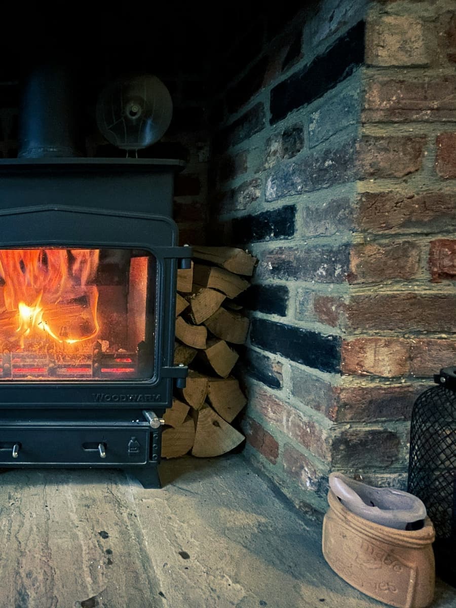 A wood stove burning in a brick alcove, with firewood stacked beside it.